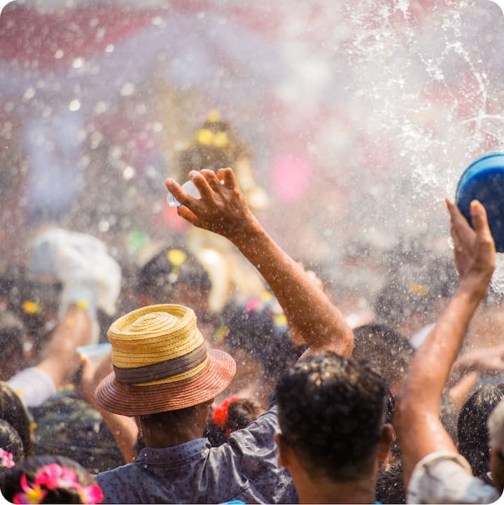 Thailand’s Songkran festival. A large group of people face away from us, arms raised, holding buckets and bottles that send water everywhere, drenching everyone.