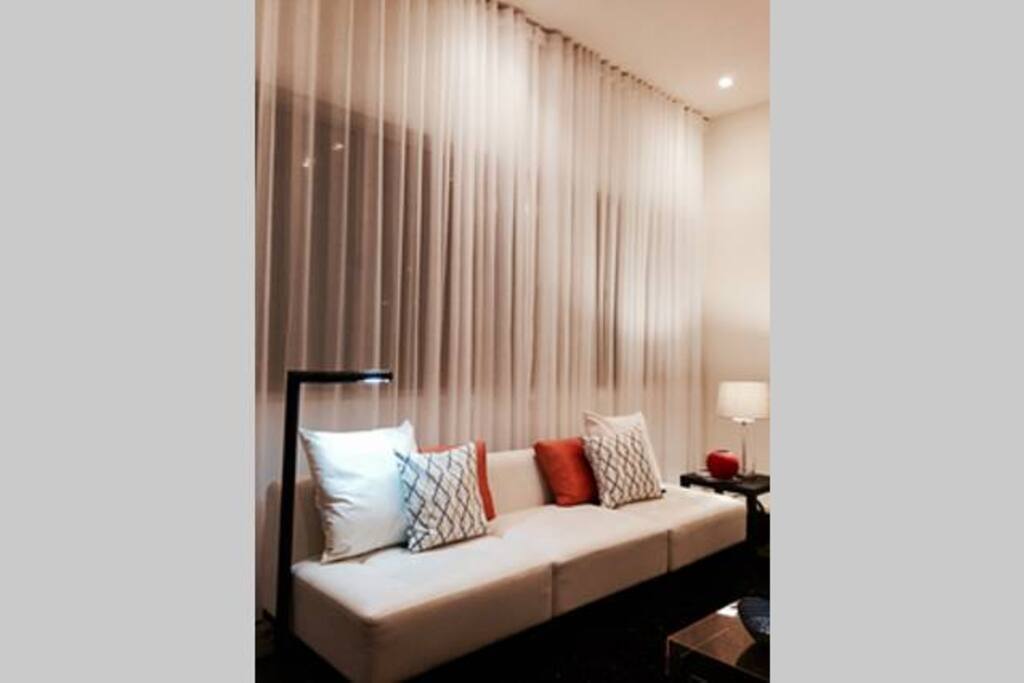 Living room has 12' ceilings with large windows and floor to ceiling sheer drapes that give it a lovely boutique setting