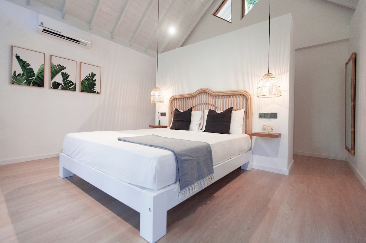 Svetlá klimatizovaná izba s vysokým stropom a posteľnou bielizňou vyzdobenou manželskou posteľou.