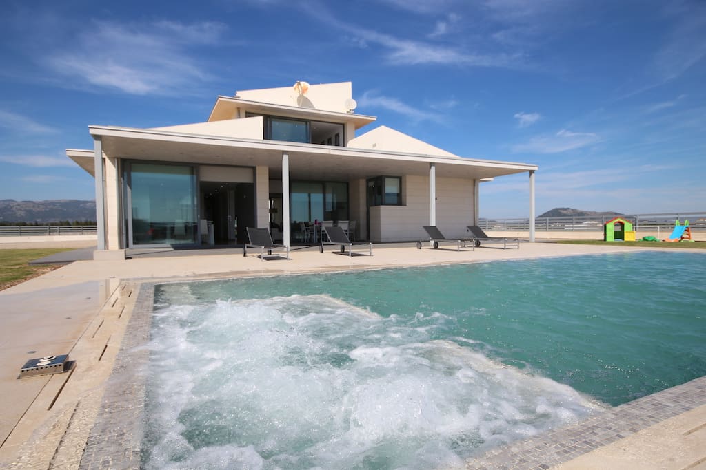 Large pool laid out, with bubbling jacuzzi, shower and modern sun beds.