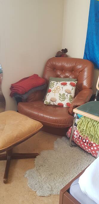In the corner, there is a cosy armchair next to a lamp, perfect for reading.
