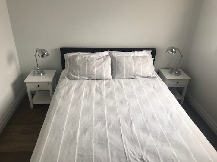Cama queen size muy cómoda a estrenar y colchón, con mesitas de noche y lámparas. El armario  se encuentra frente a la cama.