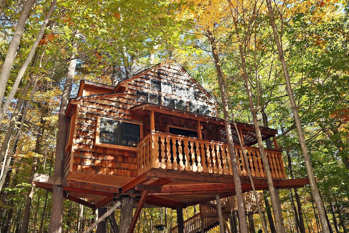 A two story New England treehouse sits among a forest with fall colors ablaze