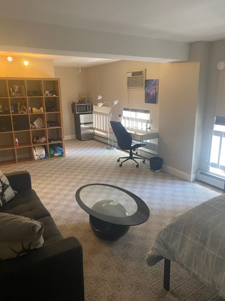 מיטת קווין נוחה בסגנון טמפורפדי עם מצעים נקיים. חדר רחצה פרטי ופינת ישיבה פרטית, שולחן קפה, חלל עבודה עם כיסא מתכוונן, מדפים בשפע ומטבחון.