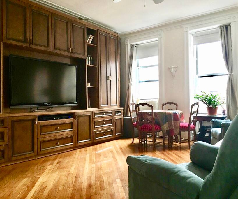 A view of the living room from the entrance. TV is 70” with enhanced speakers. Dining table expands to seat 8 guests. There is a living room coat closet and to the far left is the entrance to a full bath (shower included).
