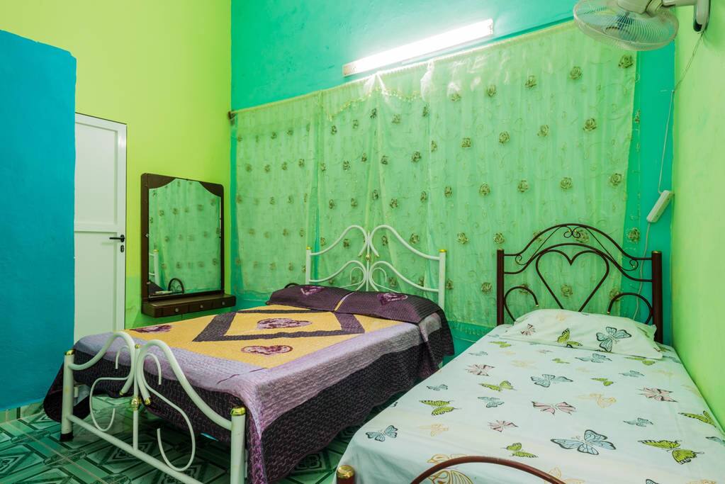 Primera habitación con capacidad para 3 personas, una cama matrimonial grande y una individual, climatizada y con ventiladores, tocador para guardar pertenencias, maquillaje etc., perchas para ropa y baño privado.