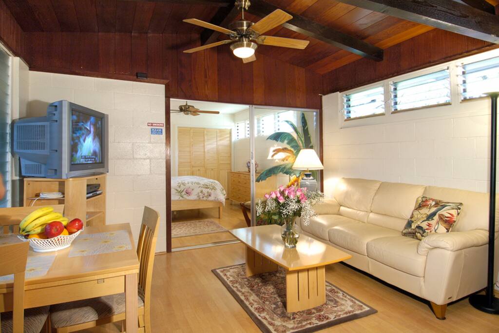 Picture of the main room towards the larger first bedroom with a queen size bed. The two rooms are separated by a sliding glass door and solid vertical blinds..
