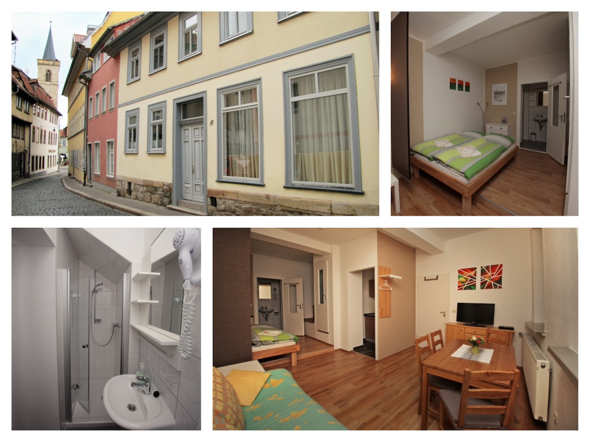 The exterior of a traditional building is shown, featuring a colorful façade with large windows. A cobblestone street adjoins the structure, creating a serene atmosphere. The interior images display a well-lit living area with a dining table, a cozy sleeping area, and a modern bathroom equipped with a shower.