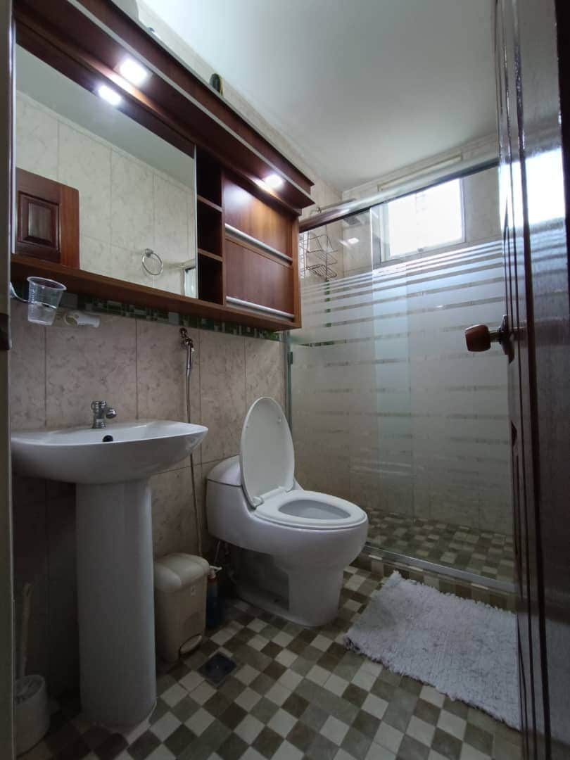 The bathroom features a glass-enclosed shower with modern fixtures. A pedestal sink is positioned beside a toilet, and wall-mounted cabinetry offers storage space. Soft lighting highlights the neutral tilework and patterned floor, enhancing the room's functionality and cleanliness.