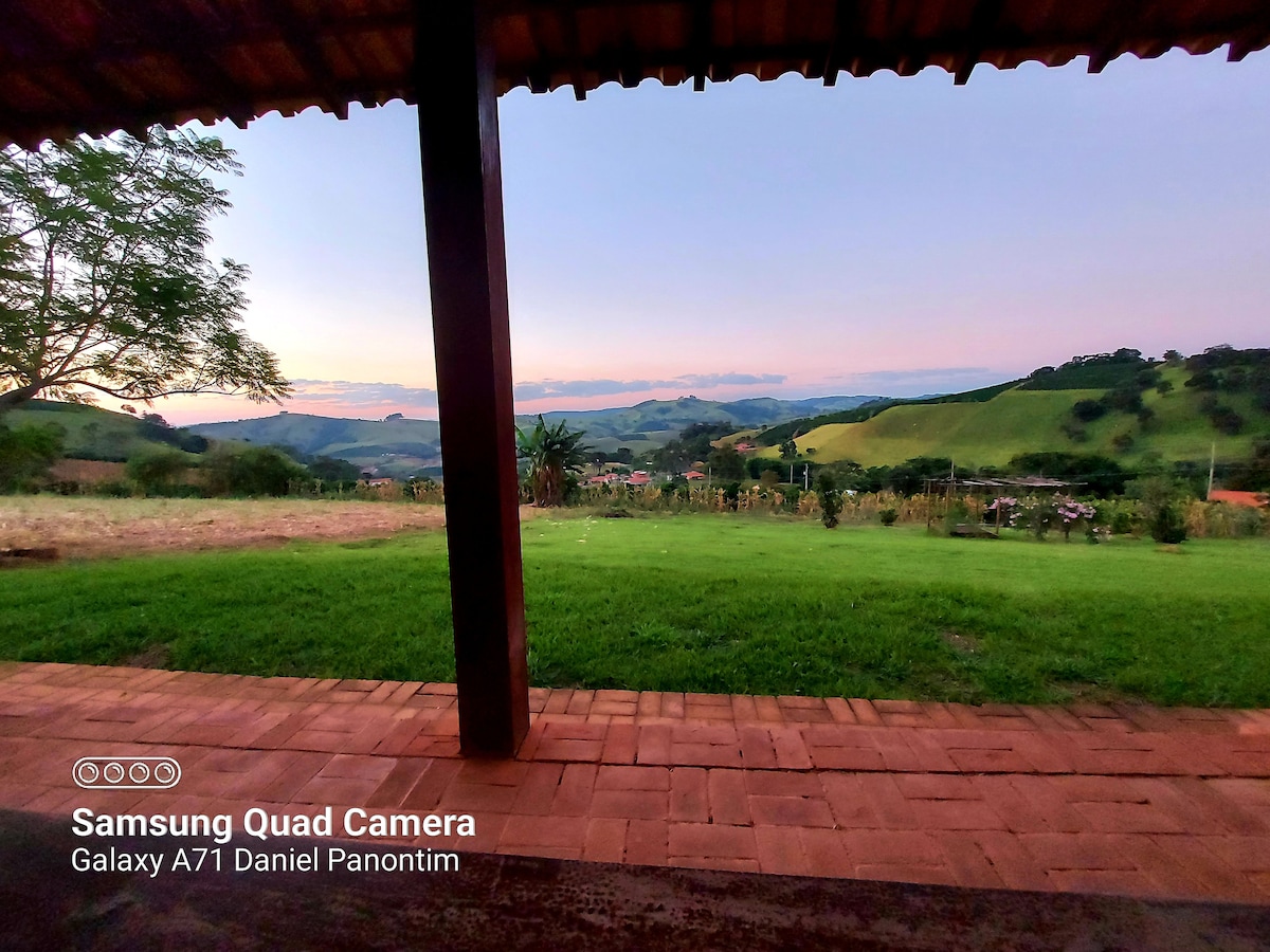 A tranquil outdoor view captures rolling green hills under a soft, pastel sky at dusk. The scene is framed by the eave of a covered porch, providing a sense of calm and connection to nature.