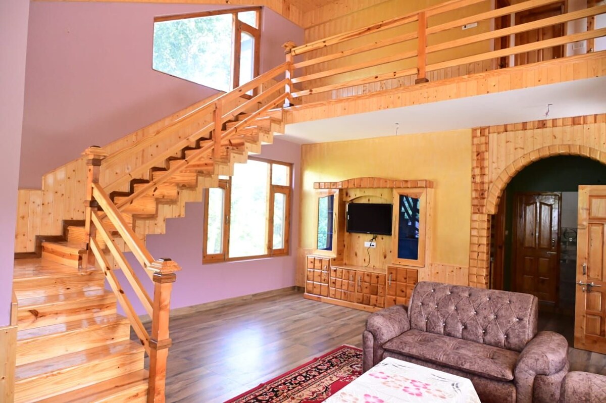 An open living space features a wooden staircase leading to a second level, with large windows allowing natural light to fill the area. A comfortable couch is situated in front of a wooden entertainment unit. The walls are adorned with warm, inviting colors.