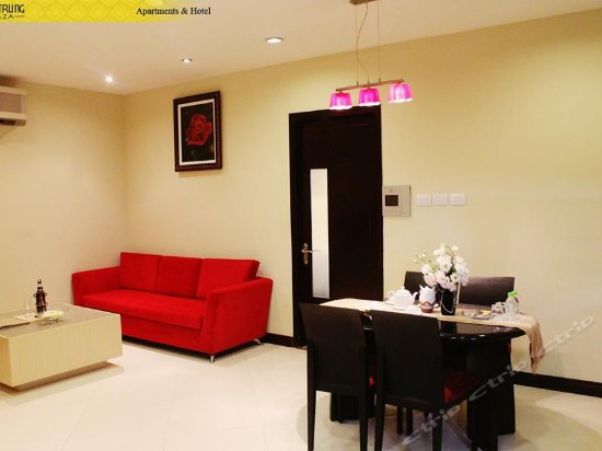 A modern living area is showcased with a bright red sofa and a dining table set for four. The walls are painted in neutral tones, while subtle lighting and artwork enhance the ambiance. A doorway leads to another space, contributing to the overall openness.