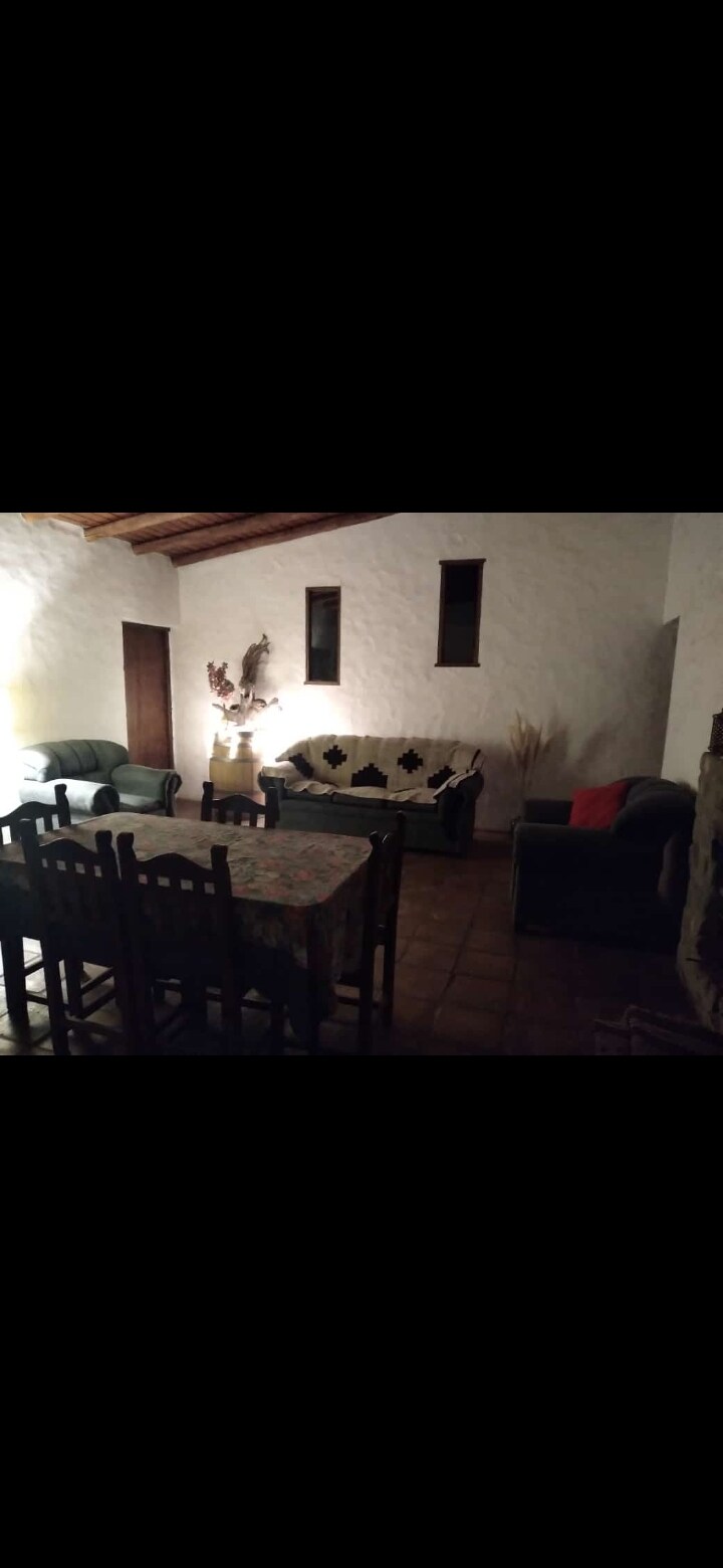 A living and dining area is visible, featuring a wooden dining table surrounded by chairs. A sofa set, including a dark green couch and a lighter couch adorned with accent pillows, is positioned near a stone fireplace. Soft lighting creates a warm ambiance.