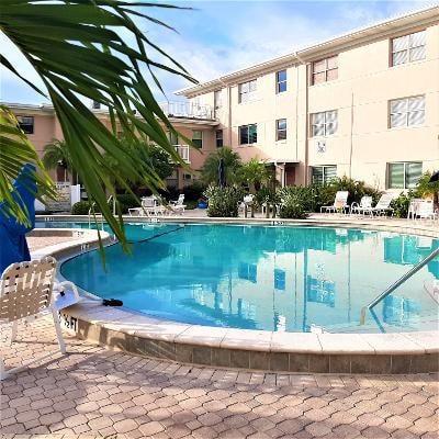 A heated pool is surrounded by a tropical courtyard, featuring lounge chairs for relaxation. Lush greenery and palm trees enhance the serene environment, while the well-maintained space invites guests to enjoy sunny days by the water.