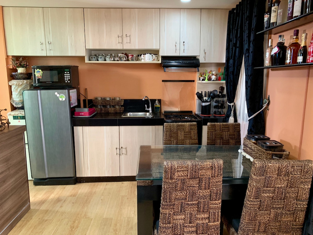 A well-equipped kitchen is shown, featuring wooden cabinetry and a glass dining table surrounded by wicker-style chairs. Counter space is available for meal preparation, complemented by a stove and sink. Various kitchen appliances are neatly arranged on the counter, enhancing functionality.