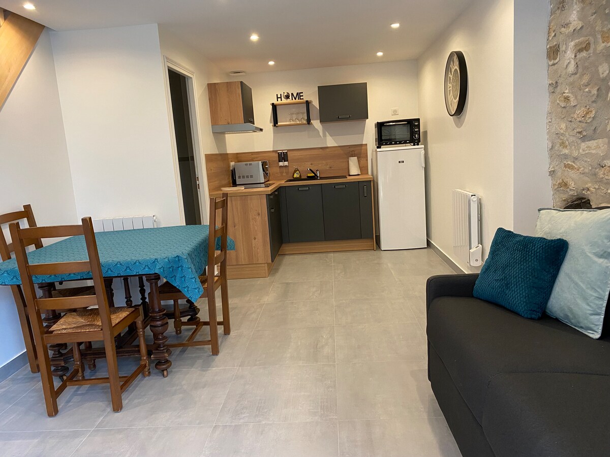 An open living area features a wooden dining table with a vibrant blue tablecloth, accompanied by four chairs. A modern kitchen is equipped with gray cabinets, a microwave, and a refrigerator. A comfortable sofa with decorative cushions enhances the inviting space.