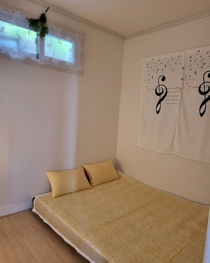 Quarto pequeno - roupa de cama grande (colchões de 9 zonas) é preparada de forma aconchegante. Luzes e ventiladores de Hanji ao lado. Há uma escada (2023,8)