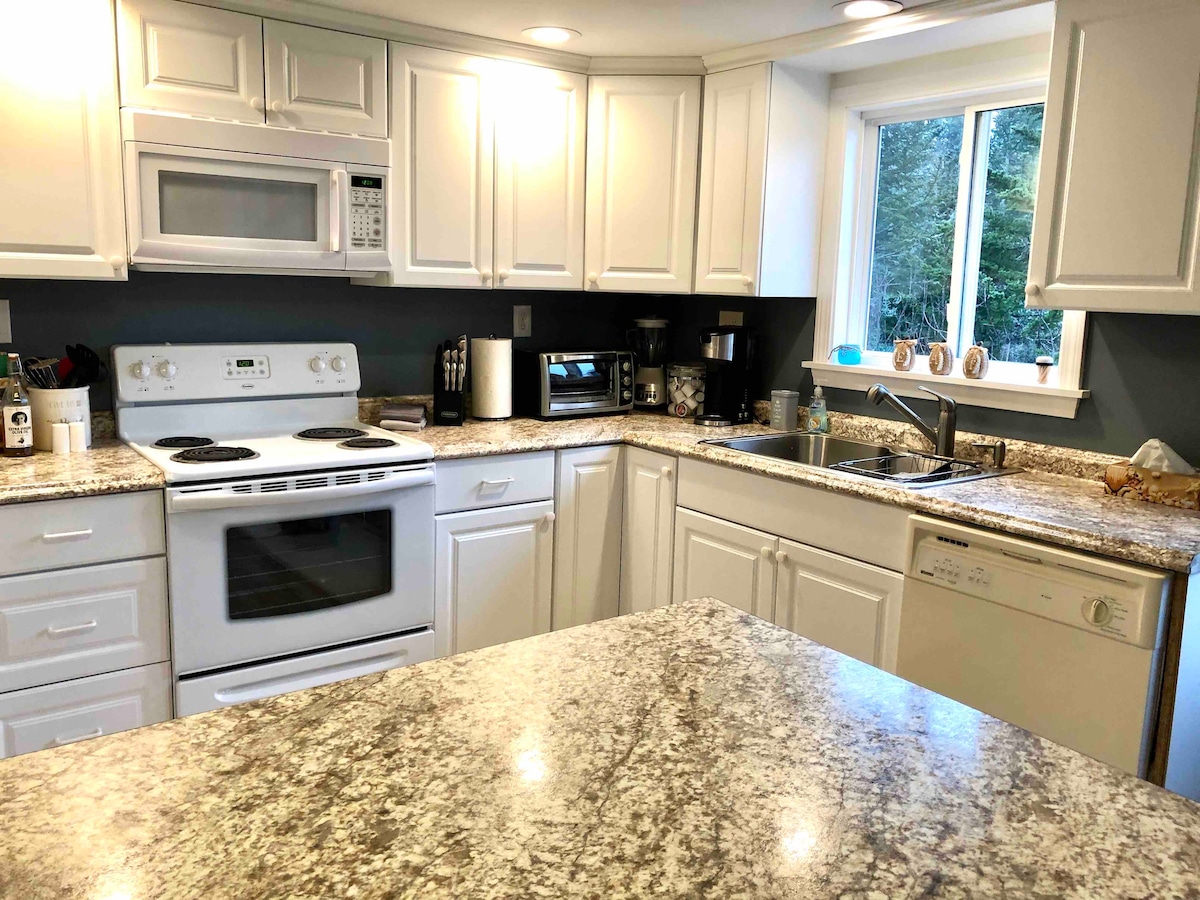 A well-equipped kitchen features white cabinetry and granite countertops. Essential appliances include an oven, microwave, refrigerator, and dishwasher. A sink is positioned beneath a window, allowing natural light to illuminate the space. Countertop space is available for meal preparation.