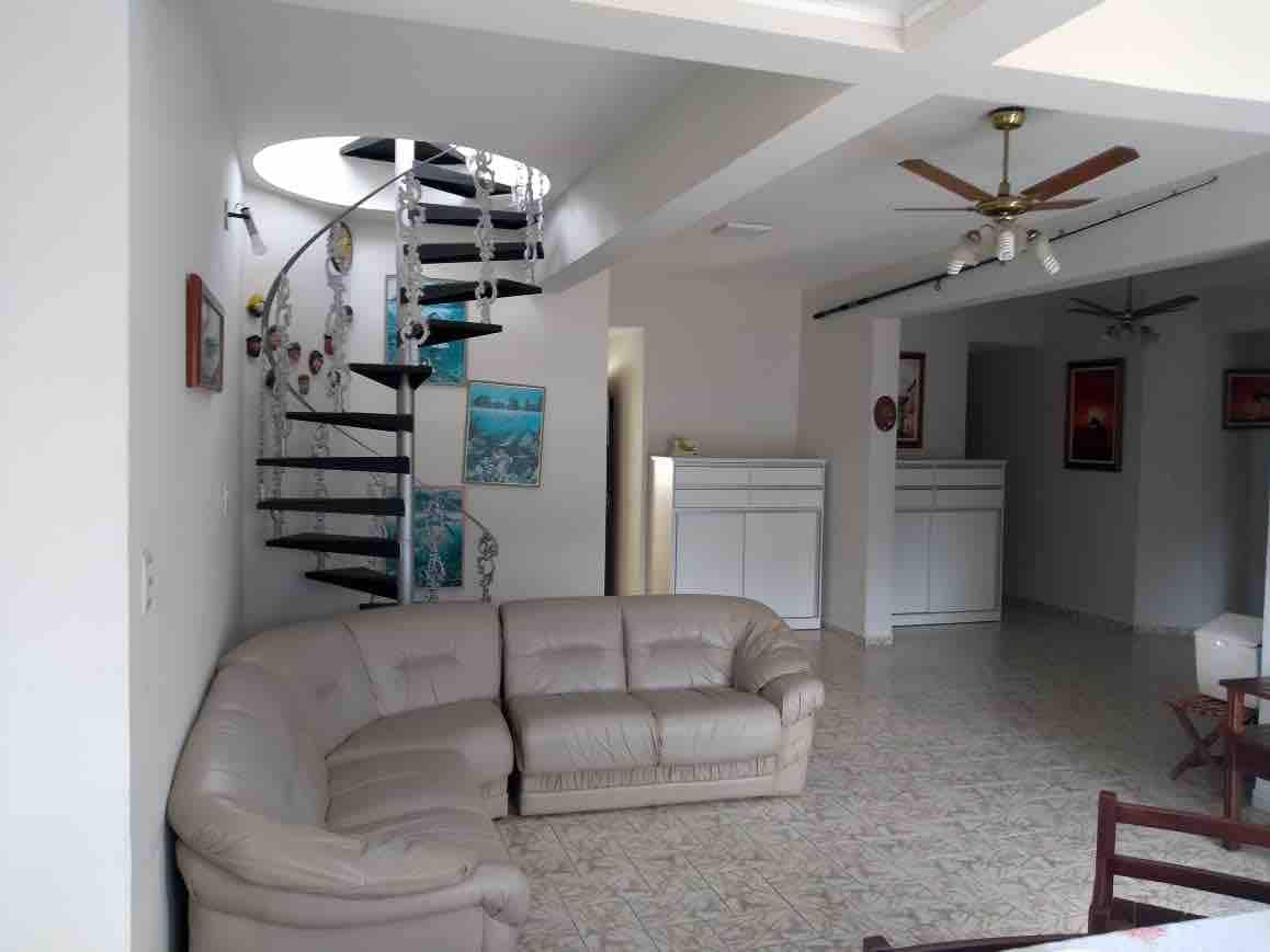 A spacious living area is highlighted by a light-colored sectional sofa. A spiral staircase leads to an upper level, complementing the neutral color palette. Decorative wall art adds character, and large windows allow natural light to fill the room.