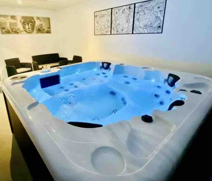 A spacious spa is prominently featured, showcasing multiple seating areas with water jets. Soft blue water creates a calming atmosphere, complemented by modern black furniture positioned nearby. Minimalistic wall art enhances the contemporary decor, adding a serene touch to the wellness space.