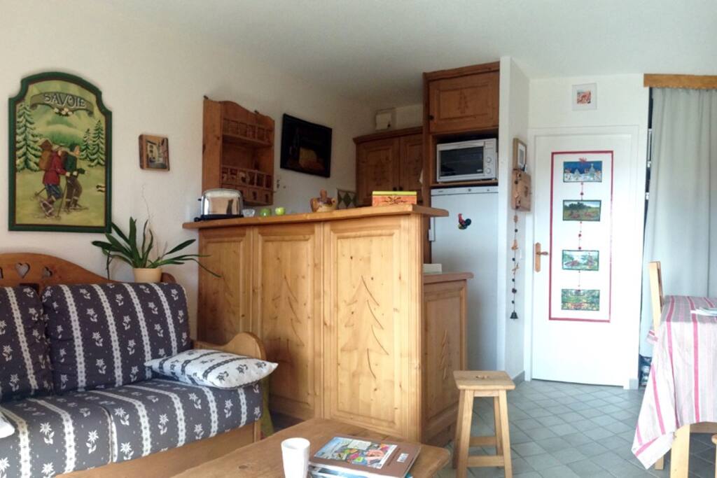 Salle de vie avec canapé-lit, mobilier motif cœur et sapin, grande table (2 rallonges en plus), 2 chaises, 2 tabourets. Accès terrasse