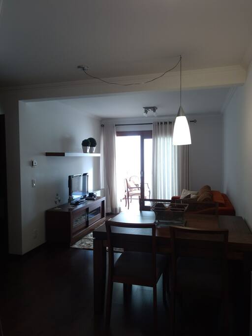 Sala com sofá cama de casal, mesinhas laterais, mesa com quatro cadeiras, rack com TV, cristaleira, tapete e cortinas.
Sacada com duas cadeiras, churrasqueira,pia e balcão.