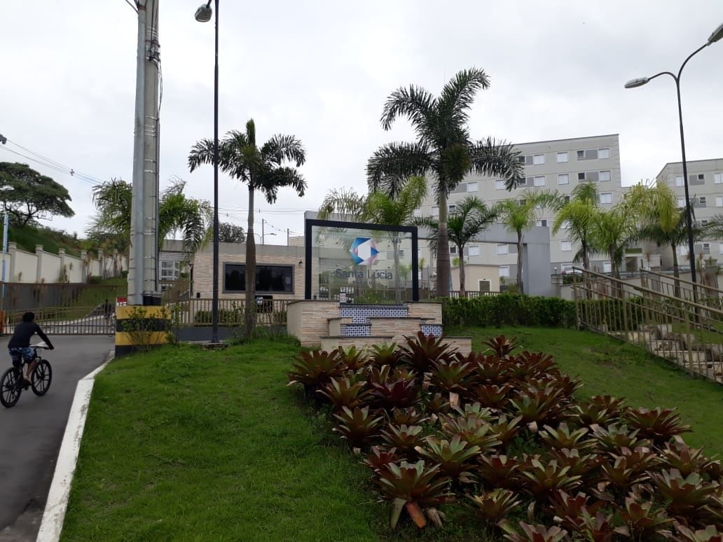 The entrance of the condominium is marked by a contemporary sign featuring a geometric design. Lush green landscaping surrounds the area, including tall palm trees and colorful shrubs. A pedestrian pathway leads up to the entrance, providing clear access to the building.