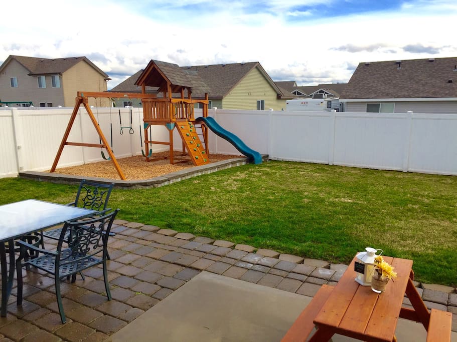 Fully fenced backyard with BBQ, Playset, and dining table.
