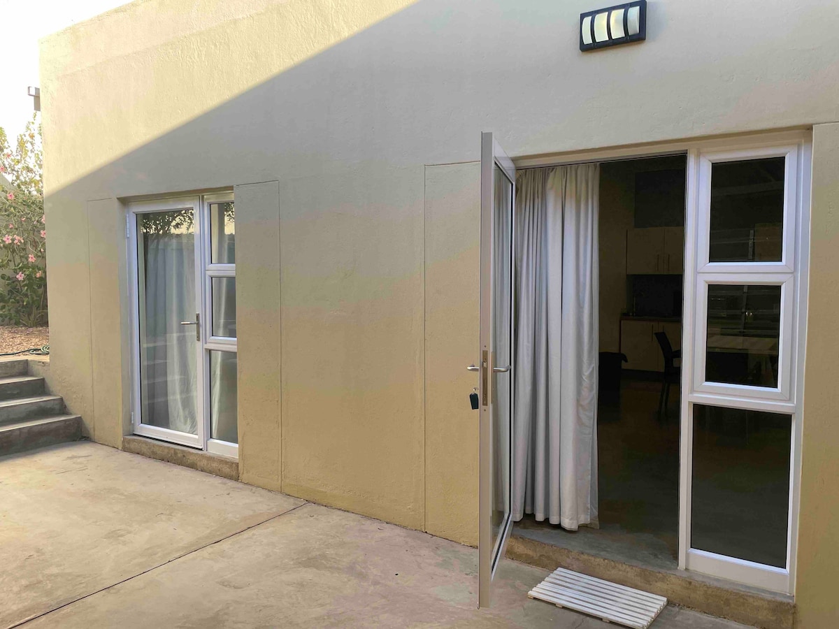 Two large glass doors provide access to a serene outdoor area, framed by light-colored walls. The doors' design includes multiple panes, allowing natural light to softly illuminate the adjacent space, where light-colored curtains gently hang.