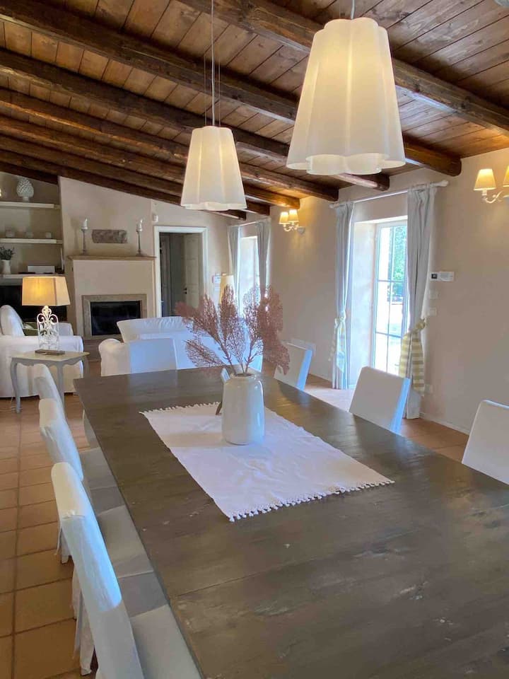 Grand salon avec coin repas intérieur, 2 canapés-lits, cheminée en pierre, 2 portes-fenêtres et grande fenêtre sur le jardin du domaine