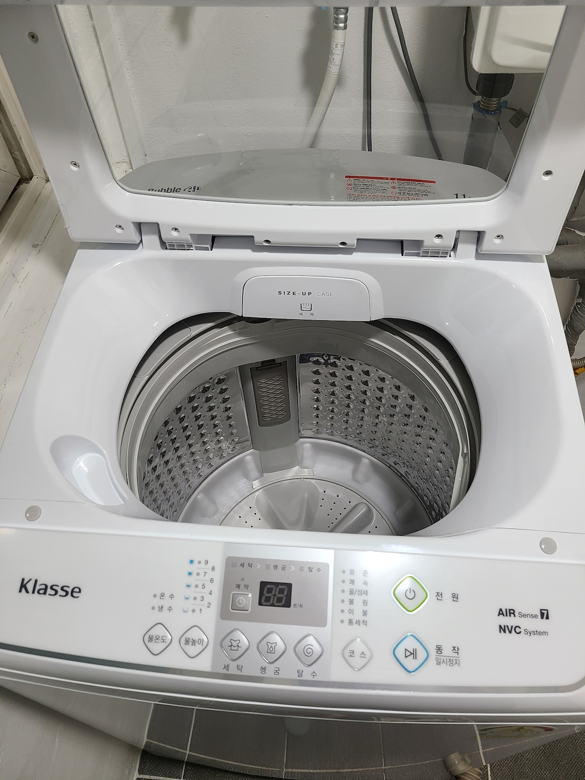 The image showcases a top-loading washing machine with a clear lid, revealing a spacious drum inside. The control panel is located at the front, featuring buttons and a digital display for ease of use. The overall design reflects a modern and functional appliance.