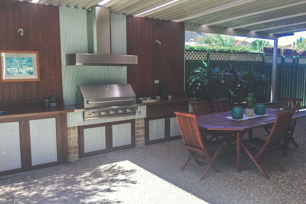 huge covered outdoor built-in bbq area with seating for 8, small bar fridge and sink.