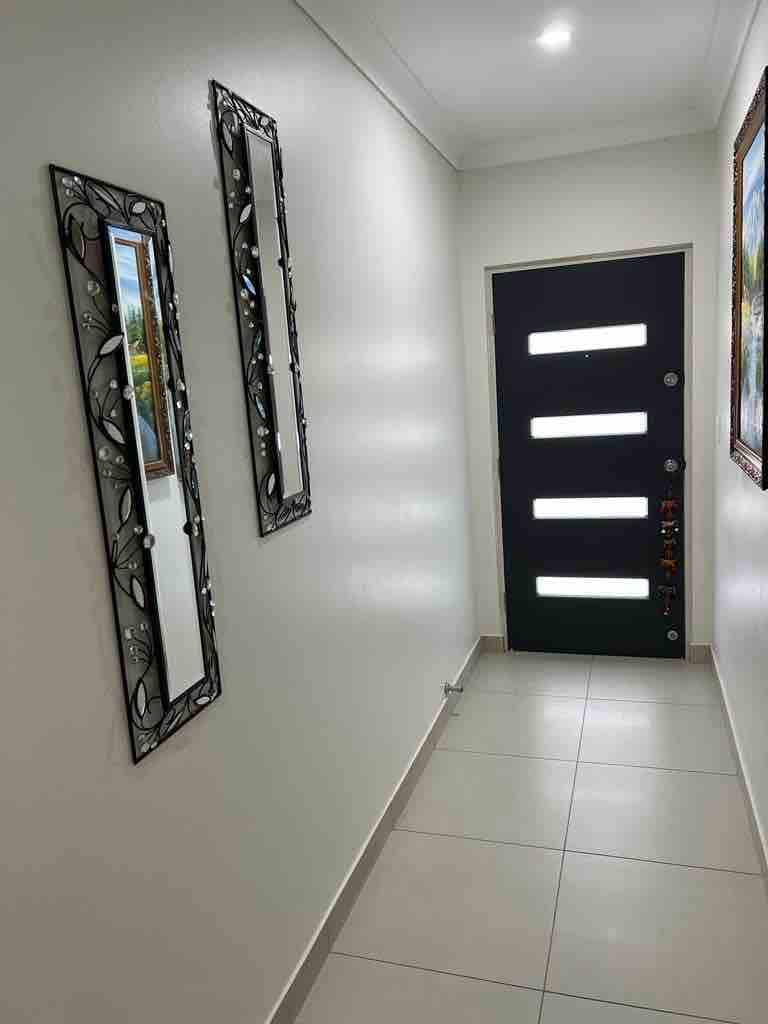 A well-lit hallway features two decorative mirrors framed with intricate designs, reflecting the light from the ceiling. A modern doorway with multiple vertical panels stands at the end, accompanied by a vibrant piece of artwork on the adjacent wall.