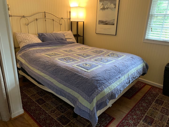Comfy Queen Bed with down comforter and quilted bedspread. Bedroom light is switched on wall and bedside. Has phone, tablet stand with USB charging ports.