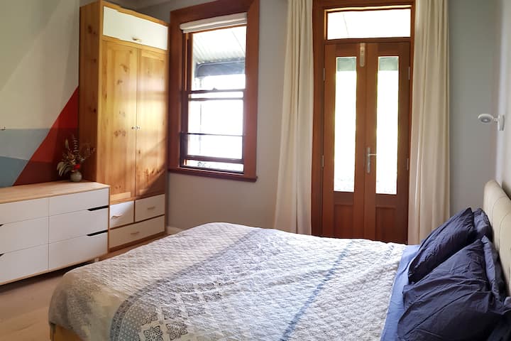 chambre principale avec salle de bain attenante, balcon et ventilateur au plafond