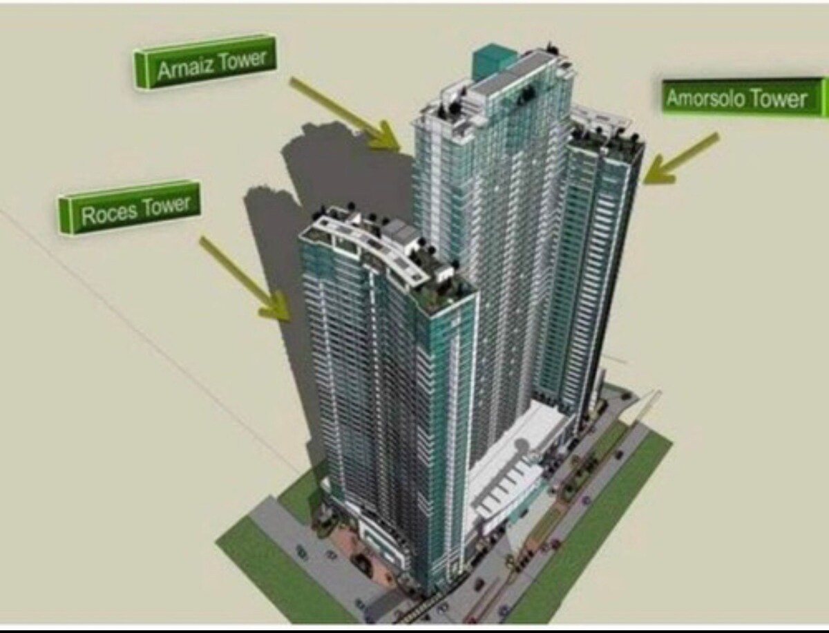 A high-rise building is depicted from an aerial perspective, featuring three distinct towers marked as Arnaiz Tower, Amorsolo Tower, and Roces Tower. The buildings exhibit a modern architectural style with expansive glass facades and numerous floors. Lush greenery surrounds the base of the structure.