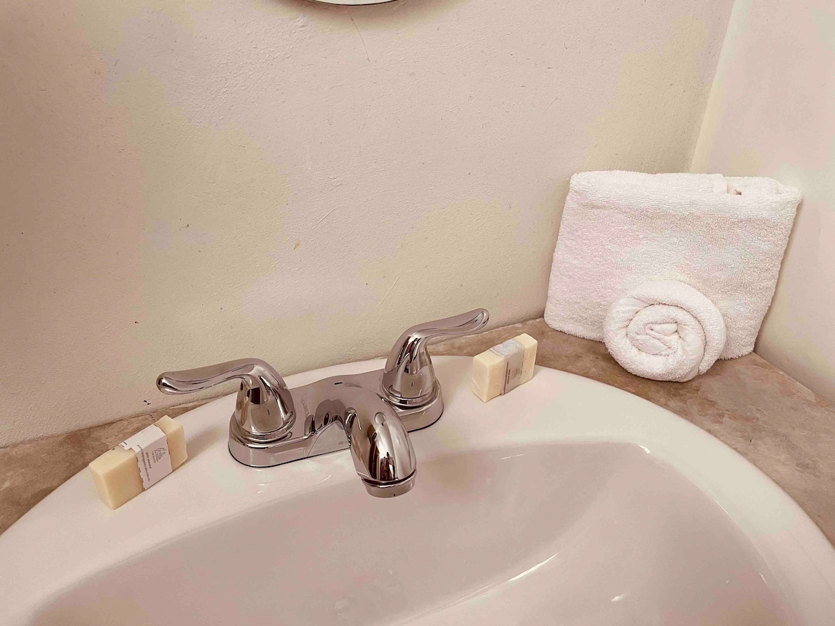 A clean bathroom countertop is displayed, featuring a chrome faucet and a white towel neatly rolled beside it. Two bars of soap are placed on the surface, contributing to a simple and functional design.