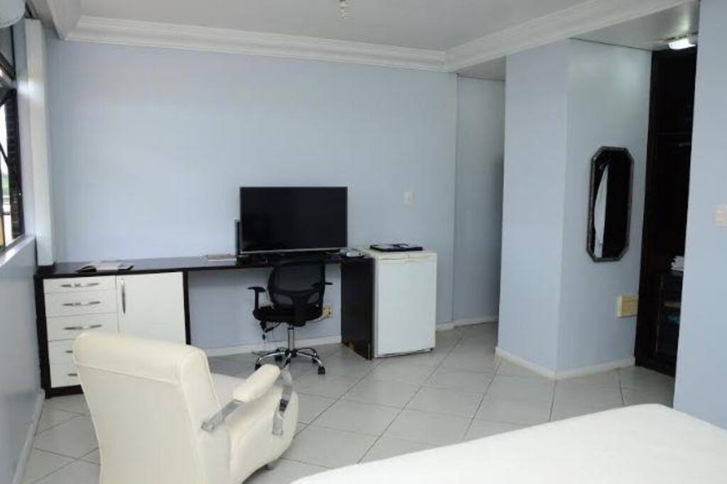 Bancada com TV flat screen, frigobar, gavetas e cadeira para usar laptop.