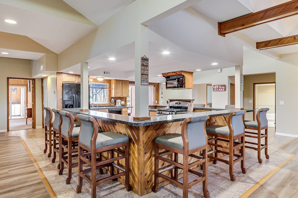 An expansive kitchen features an open floor plan with a large central island surrounded by bar seating. Wood accents and neutral tones create a spacious area equipped with modern appliances and ample counter space, enhancing the functionality for cooking and entertaining.