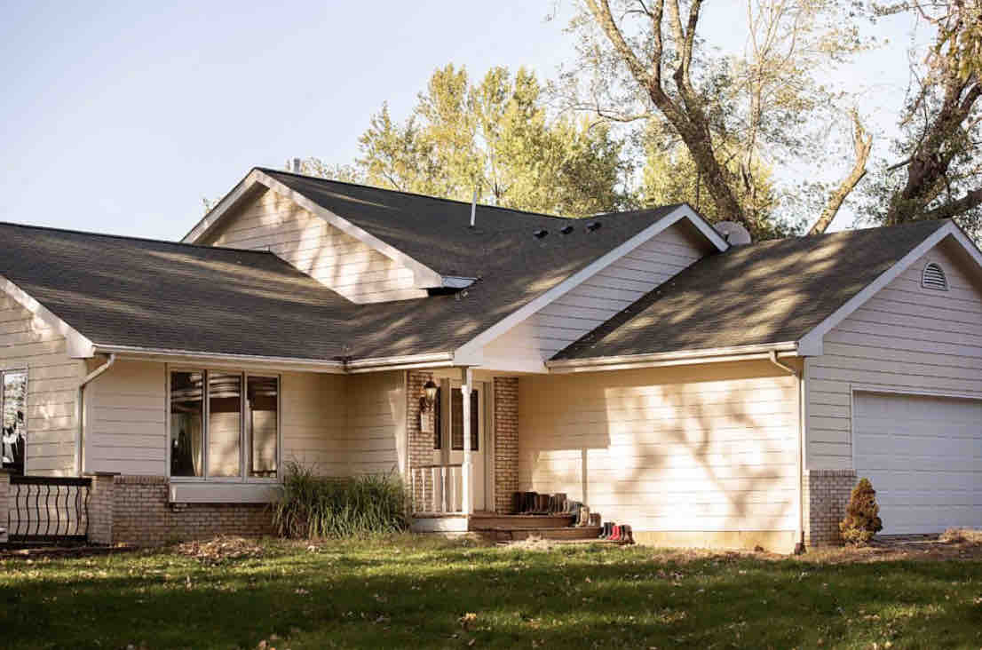 A split-level home is set amidst lush green landscaping. The exterior features a light-colored façade with a combination of brick and siding, alongside a two-car garage. Large windows allow natural light to enter, enhancing the welcoming appearance.