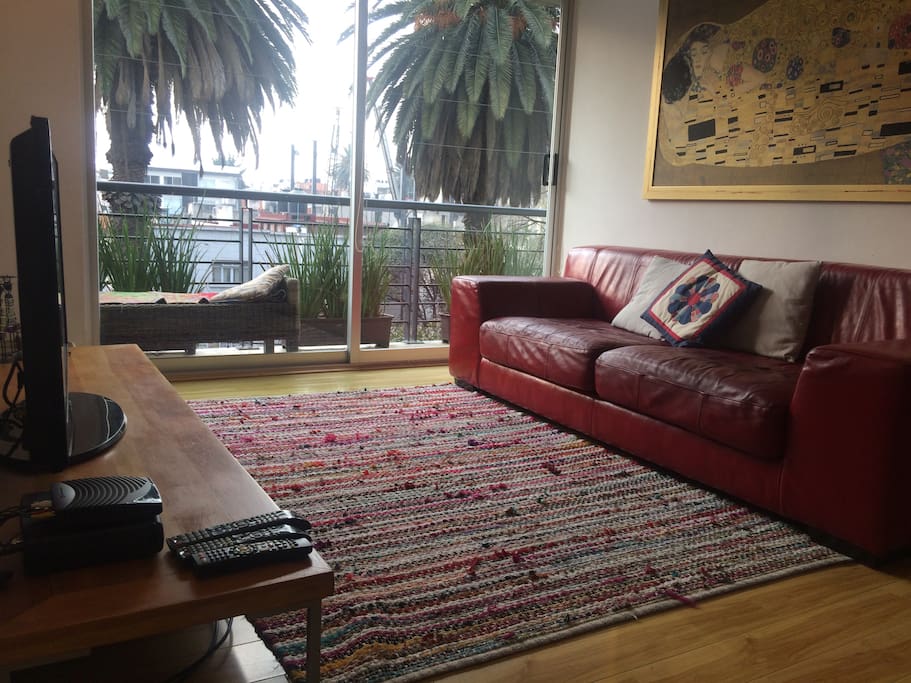 Sala estancia con decoración contemporánea, sofá de piel, tv y vista exterior y salida al balcón.