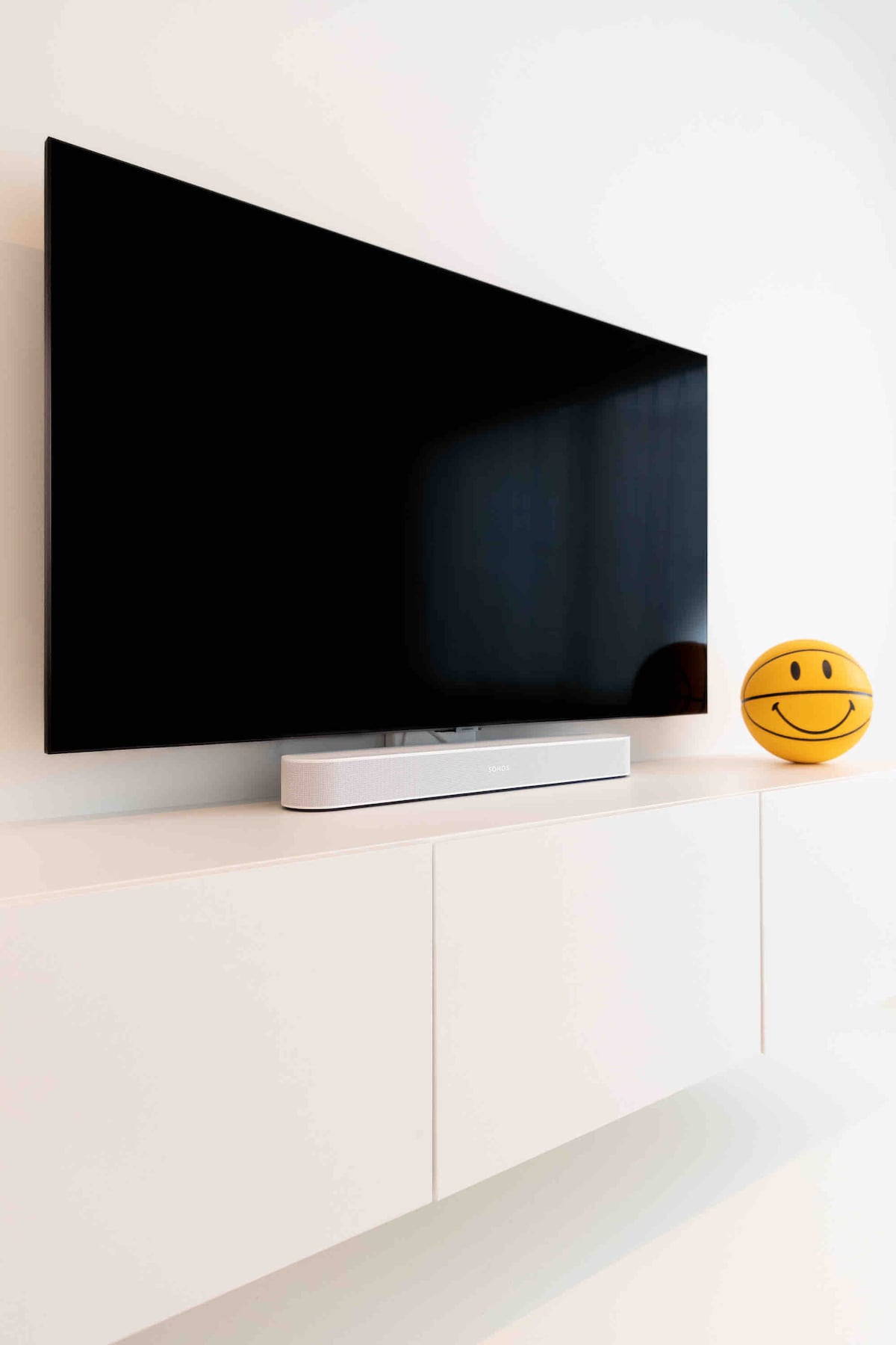A large flat-screen television is mounted on a white wall, accompanied by a sleek sound system beneath it. A cheerful smiley face decorates the side, adding a playful element to the contemporary design.