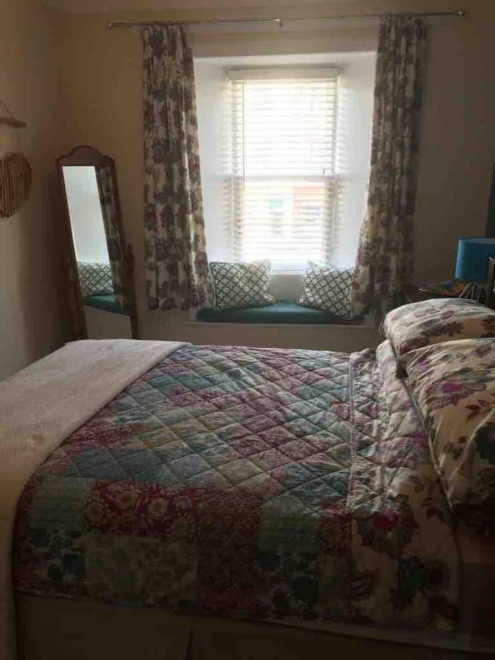 Este espacioso dormitorio tiene un baño con ducha y una lujosa cama cómoda. Las lámparas de noche se activan por  tacto y hay persianas de madera, así como cortinas en las ventanas.
