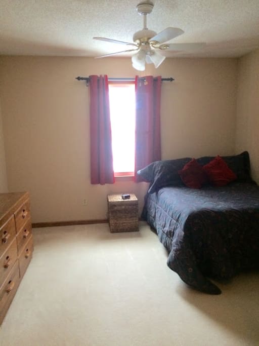 Full-sized bed with ceiling fan, dresser drawers, and attached full bath.
