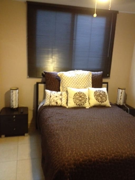 Master bedroom in apartment with new double sized bed for 2 people with 2 night tables with lamps and with 32" wall mounted cable TV, air conditioner and ceiling fan.