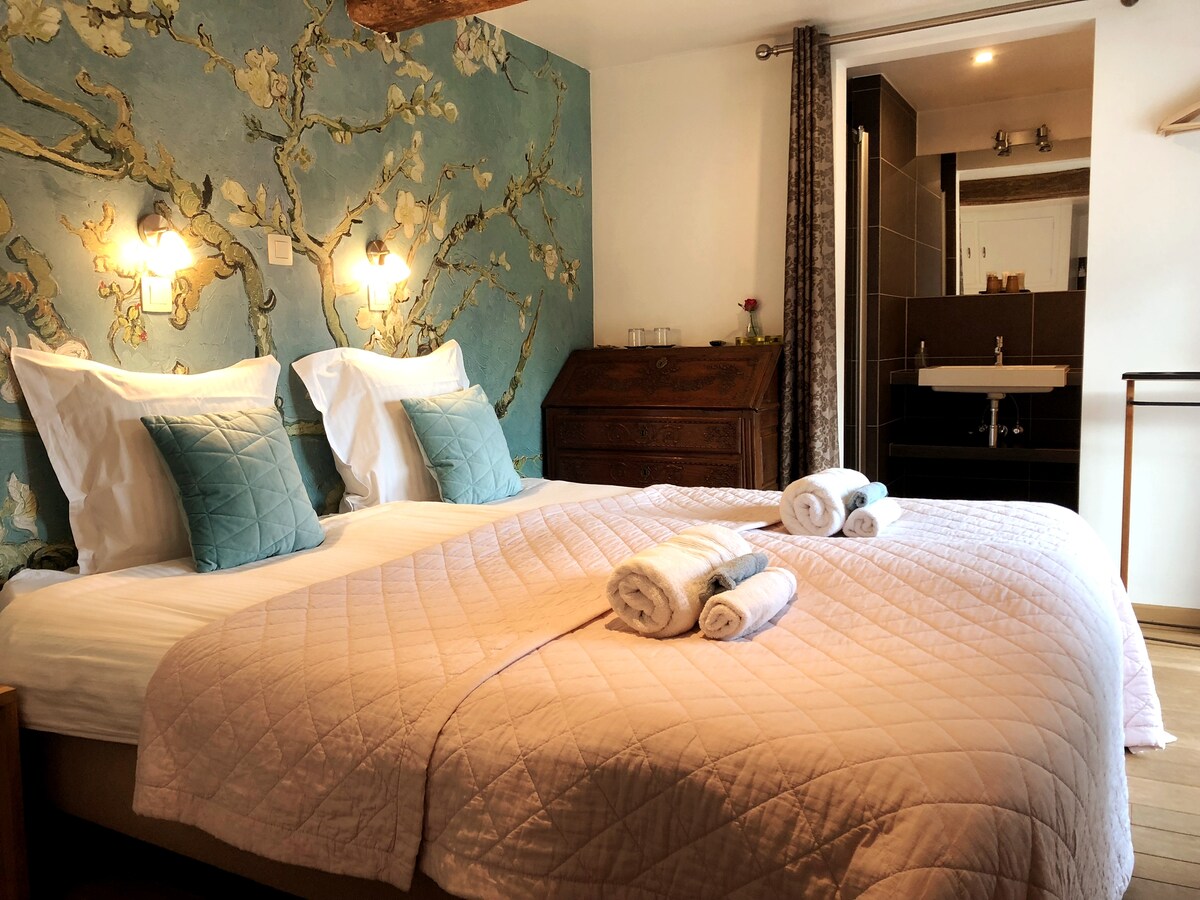 A comfortable sleeping area features two spacious beds adorned with soft, pastel-colored bedding and decorative pillows. A floral mural covers one wall, while an elegant wooden chest adds character to the room. Natural light filters in, creating a welcoming ambiance.