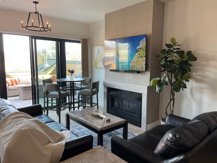 Sala de estar con TV inteligente Samsung de 65 pulgadas, chimenea y mesa de comedor.