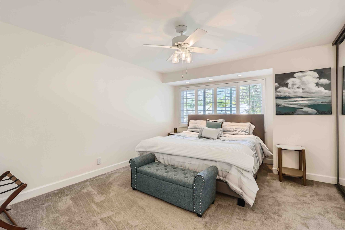 חדר שינה ראשי ענק עם מיטת קינג סייז וקיר לארון מראות מקיר, תריסי מטעים ושמיכות נעימות. 