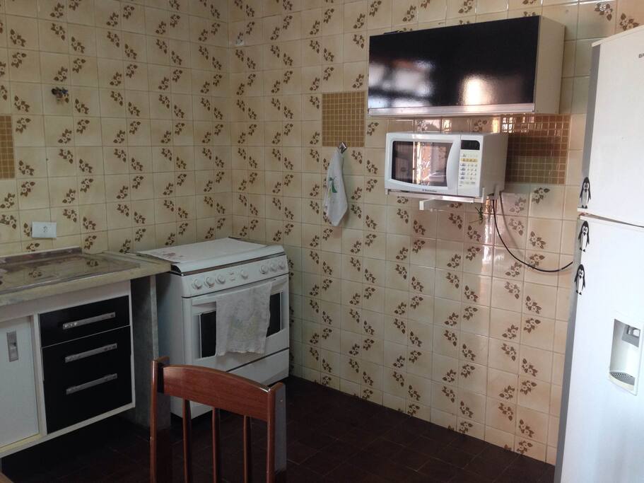 COZINHA COM GELADEIRA, FOGÃO, FORNO MICROONDAS E MESA COM 4 CADEIRAS