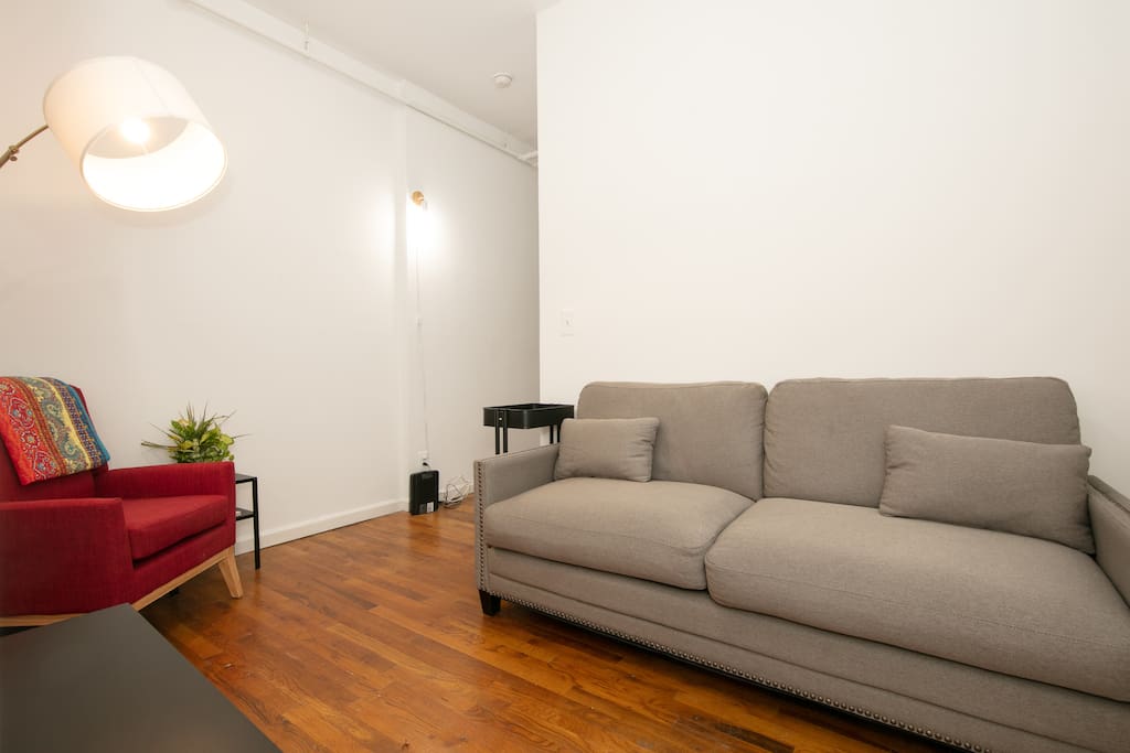 Living room area with couch and reading chair. There is now a 32inch smart TV on the black TV stand